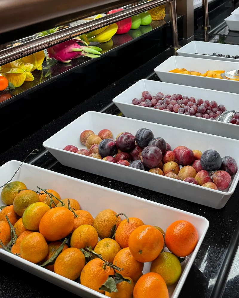 Bacs de fruits au buffet : clémentines avec leurs feuilles, prunes et raisin