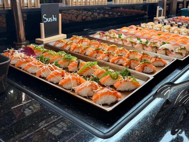 Comptoir des sushis : plateaux de sushis saumon en enfilade derrière l'ardoise « Sushi »